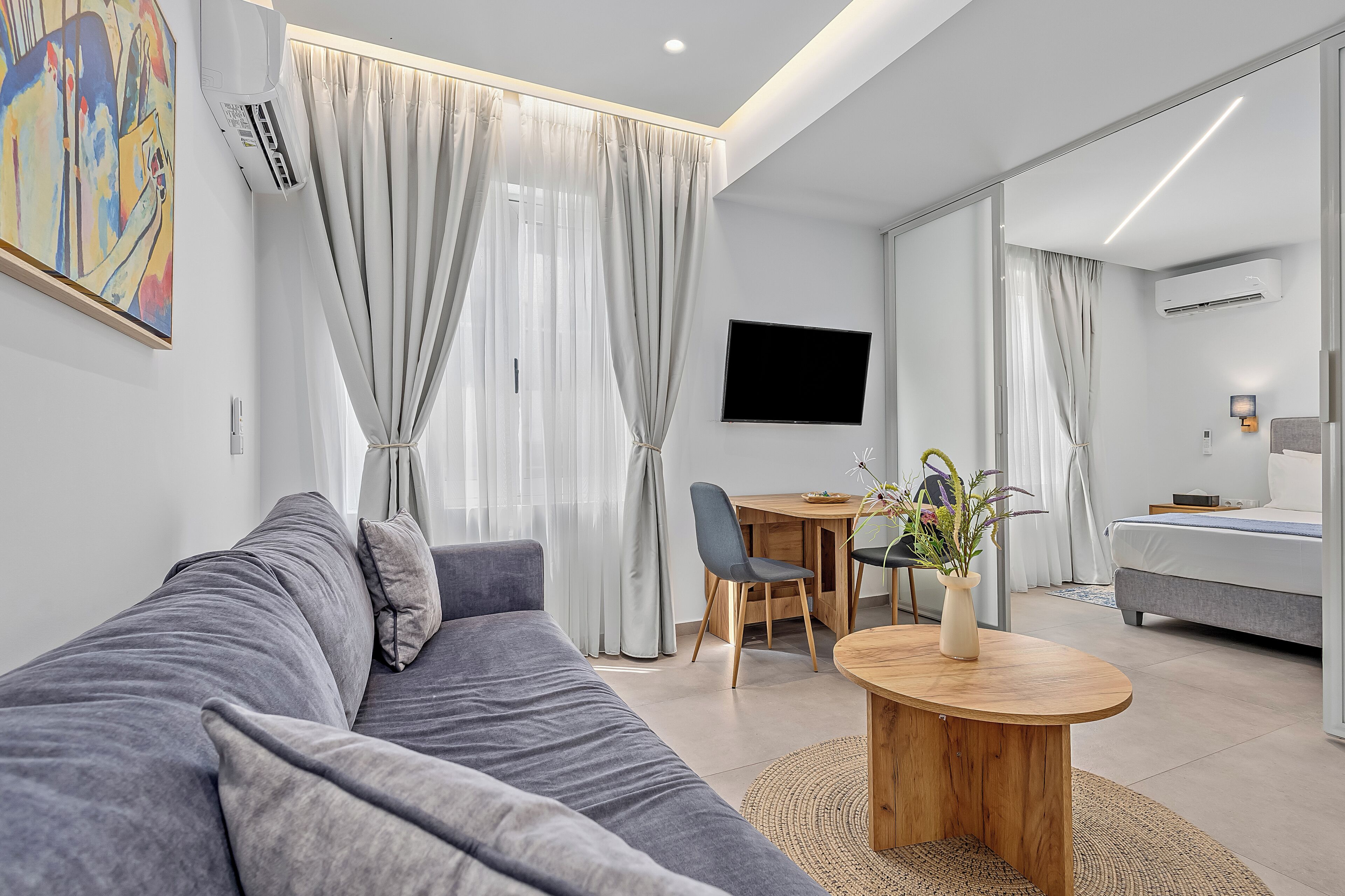 A modern living room with a grey sofa, a wooden coffee table, and a TV mounted on the wall.