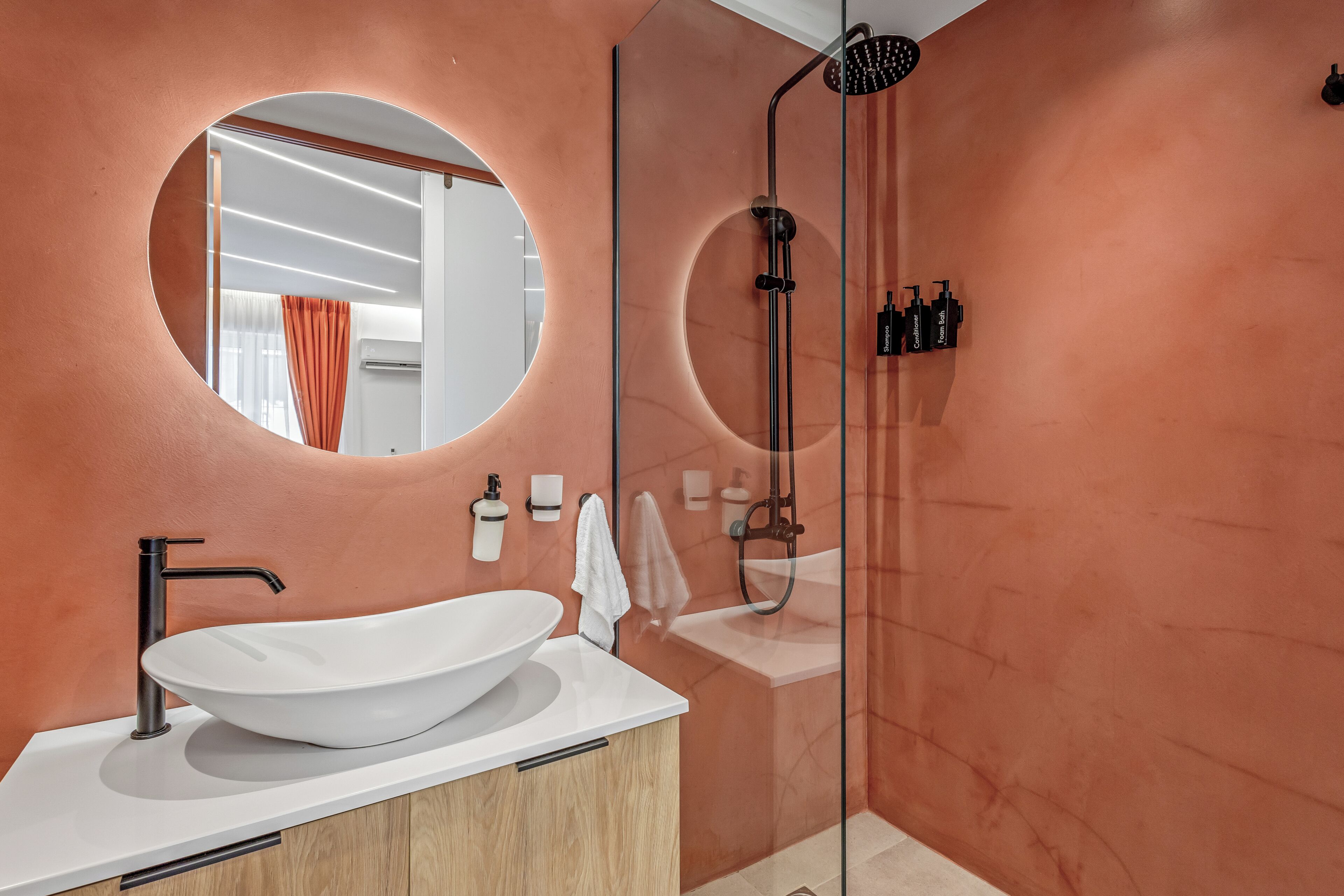 A modern bathroom with a large oval sink, a round mirror, and a glass-enclosed shower area.