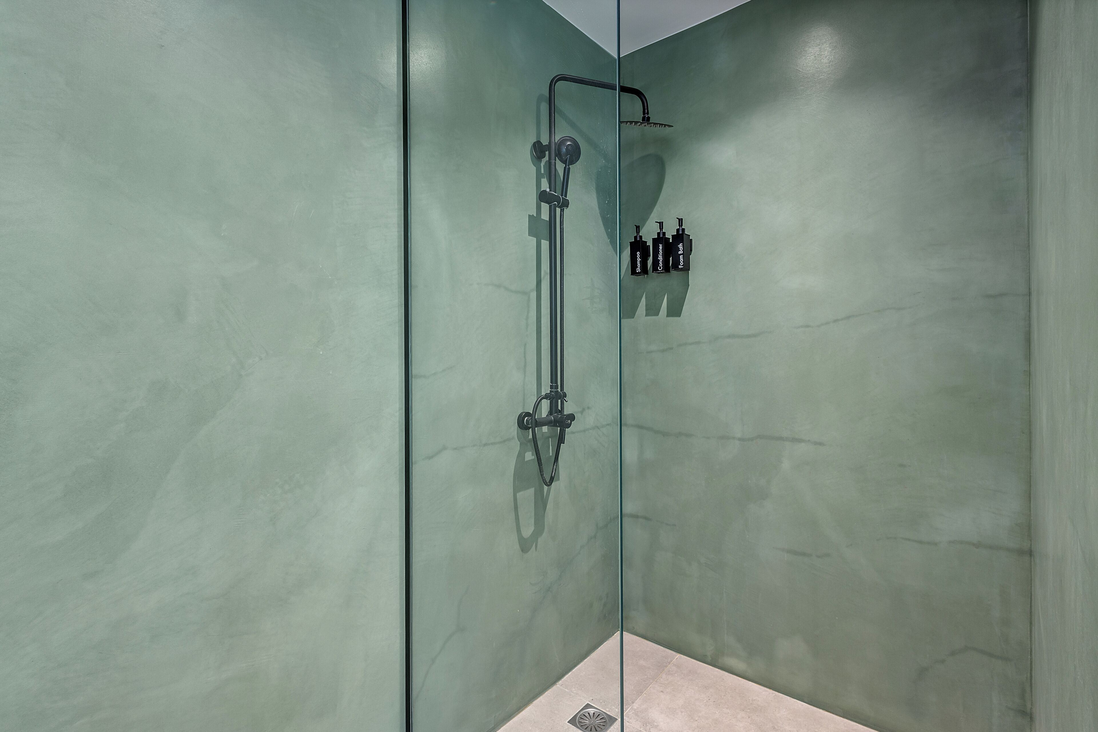 A glass-enclosed shower stall with a handheld showerhead, a handheld shower attachment, and three bottles of shampoo, conditioner, and foam bath.