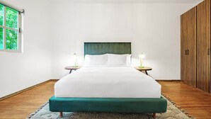 A single bed with a green upholstered headboard, two bedside tables with lamps, a wooden floor, and a window with a view of greenery. - Art Deco 2BR in Polanco  Steps to Parque Lincoln (Ciudad de México)