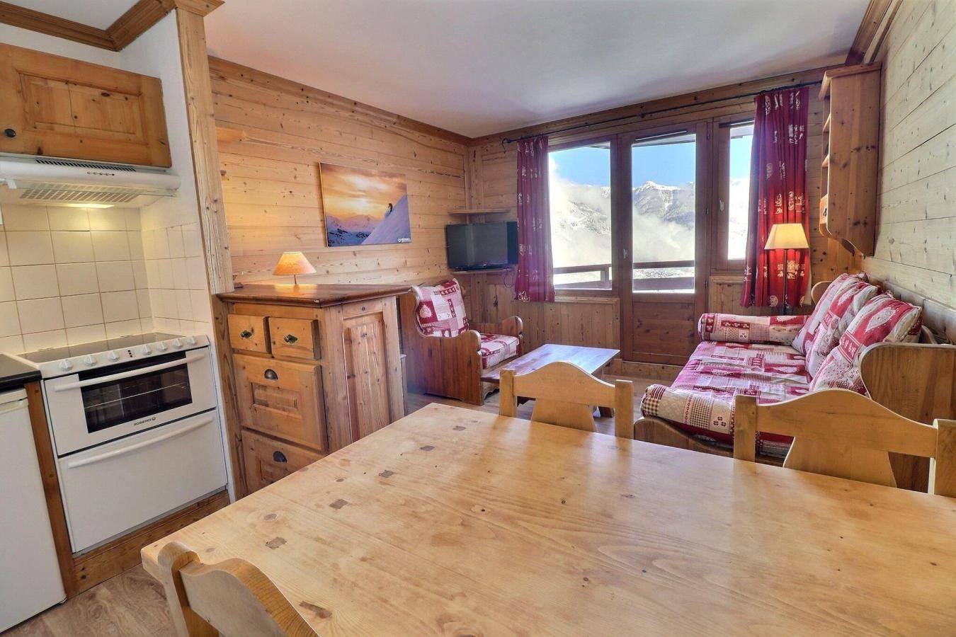 A cozy cabin-style room with a wooden interior, a dining table, a sofa, and a TV mounted on the wall.