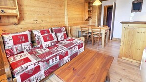 Un interior de madera acogedor con un sofá tapizado en tela estampada rojo y blanco, una mesa de comedor de madera y un armario de madera.