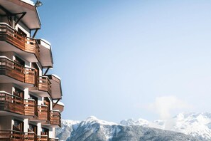 A multi-story hotel with balconies, set against a backdrop of snow-covered mountains.