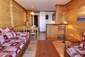 A cozy wooden cabin interior with a sofa set, a dining table, and a kitchen area.