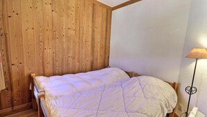 Una cama individual con edredón blanco en una habitación con paneles de madera y techo blanco.
