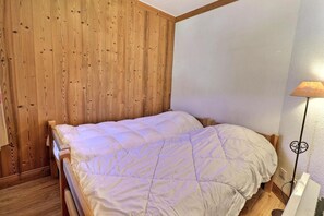 Una cama individual con edredón blanco en una habitación con paneles de madera y techo blanco.