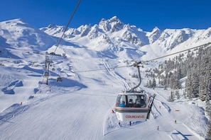 Un telesilla con el nombre 'COURCHEVEL' en el lateral, rodeado de montañas y árboles cubiertos de nieve.