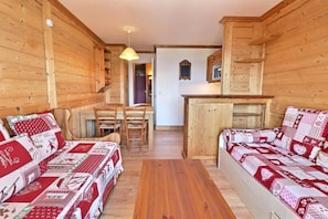 A cozy cabin interior with two wooden sofas, a dining table, and a kitchen area.
