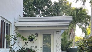 A white building with a front door, steps leading up to it, and a small porch area with potted plants. - Private Studio in the Heart of Coral Gables (Miami)