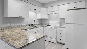A modern kitchen with white cabinets, granite countertops, a stainless steel sink, a stove, and a refrigerator. - Sea Cabins 11D - Updated Beachside Cabin, Swimming Pool, Private Beach Access! (Miramar Beach)
