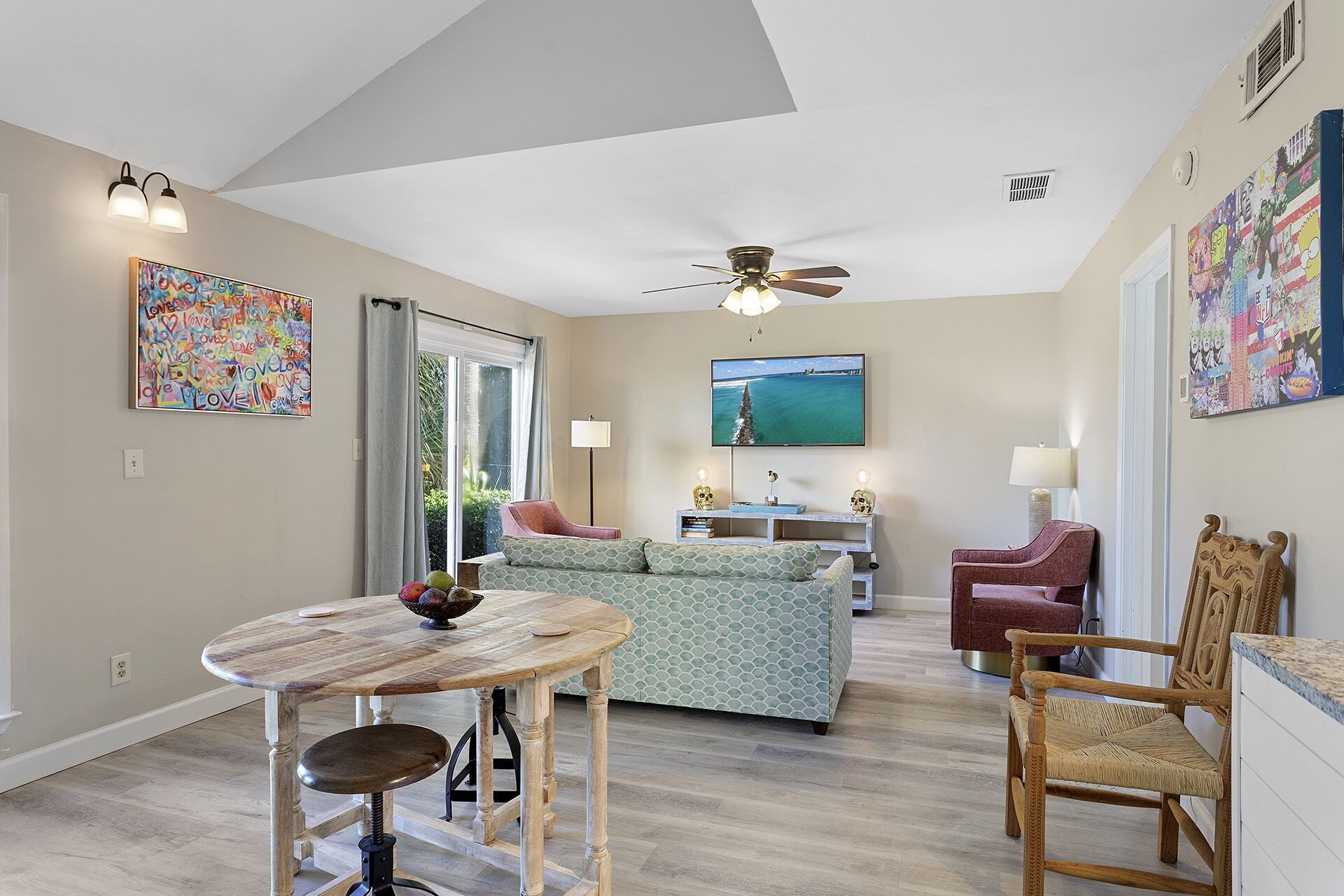 A spacious living room with a high ceiling, a ceiling fan, a large window with curtains, a sofa, a coffee table, a TV, and a red armchair.