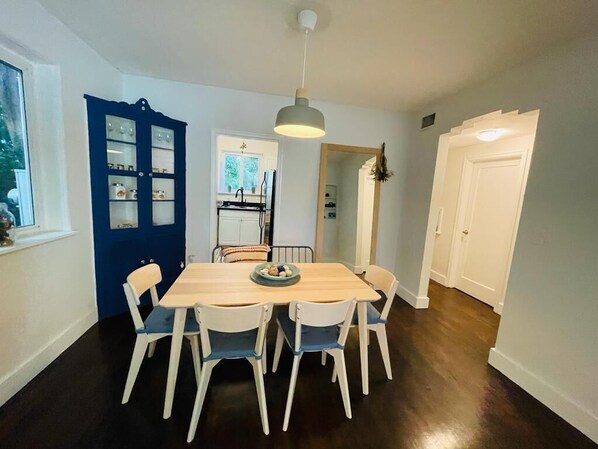 A dining area with a wooden table and white chairs, a blue cabinet with glass doors, and a hanging light fixture.
