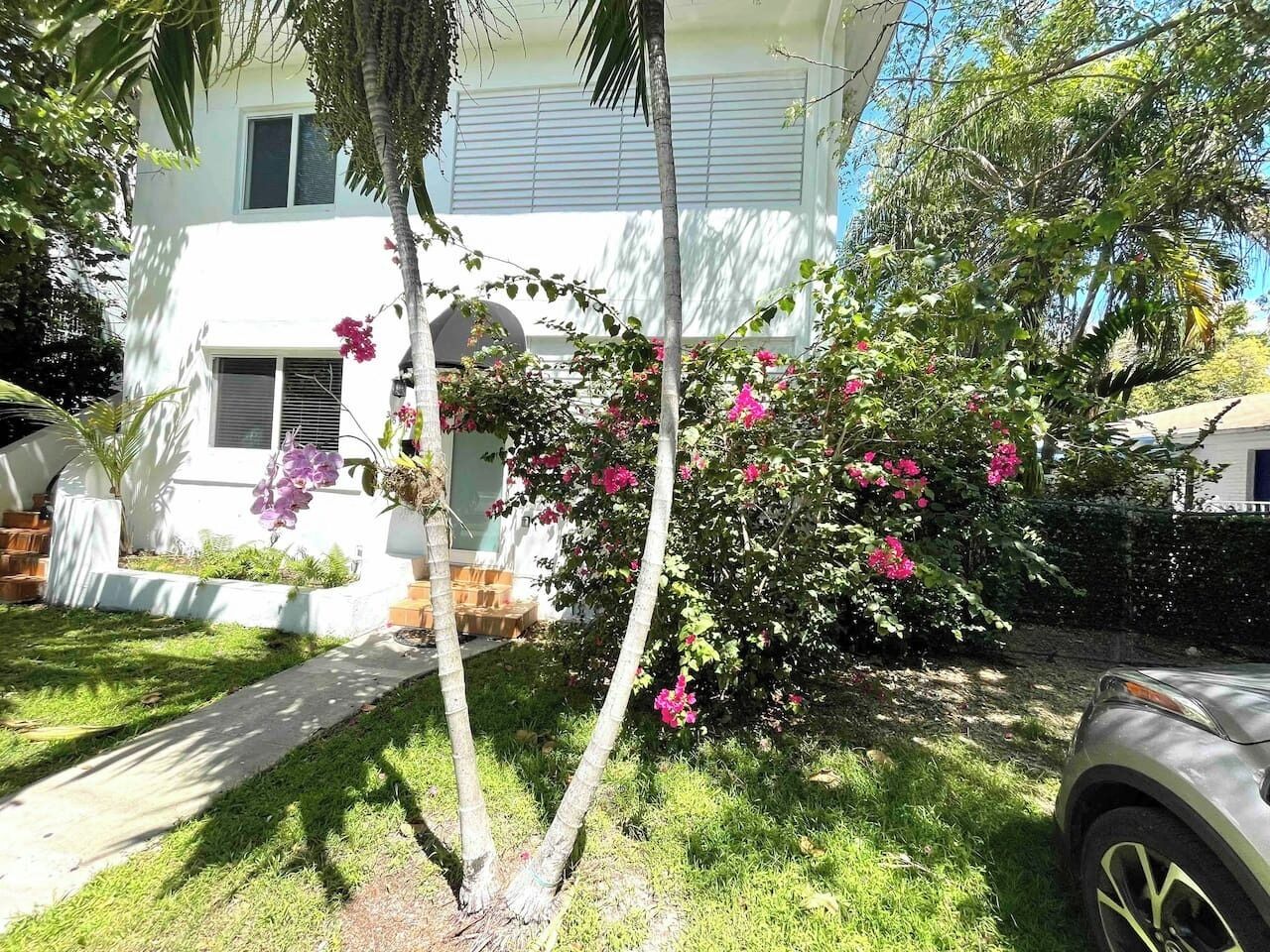 A residential building with a white exterior, a visible window, and a tree with pink flowers.