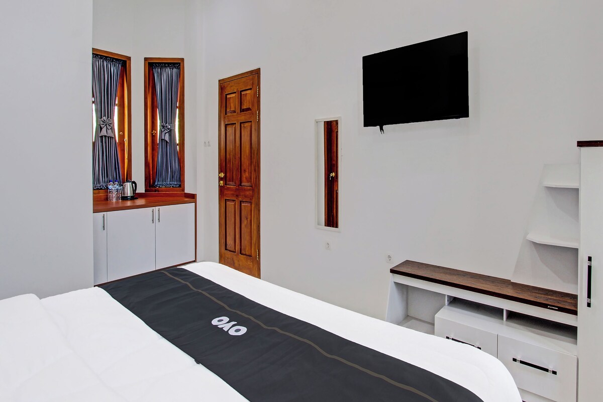 Ein Hotelzimmer mit Bett, Wandfernseher, Kleiderschrank und einem Vorhangfenster.