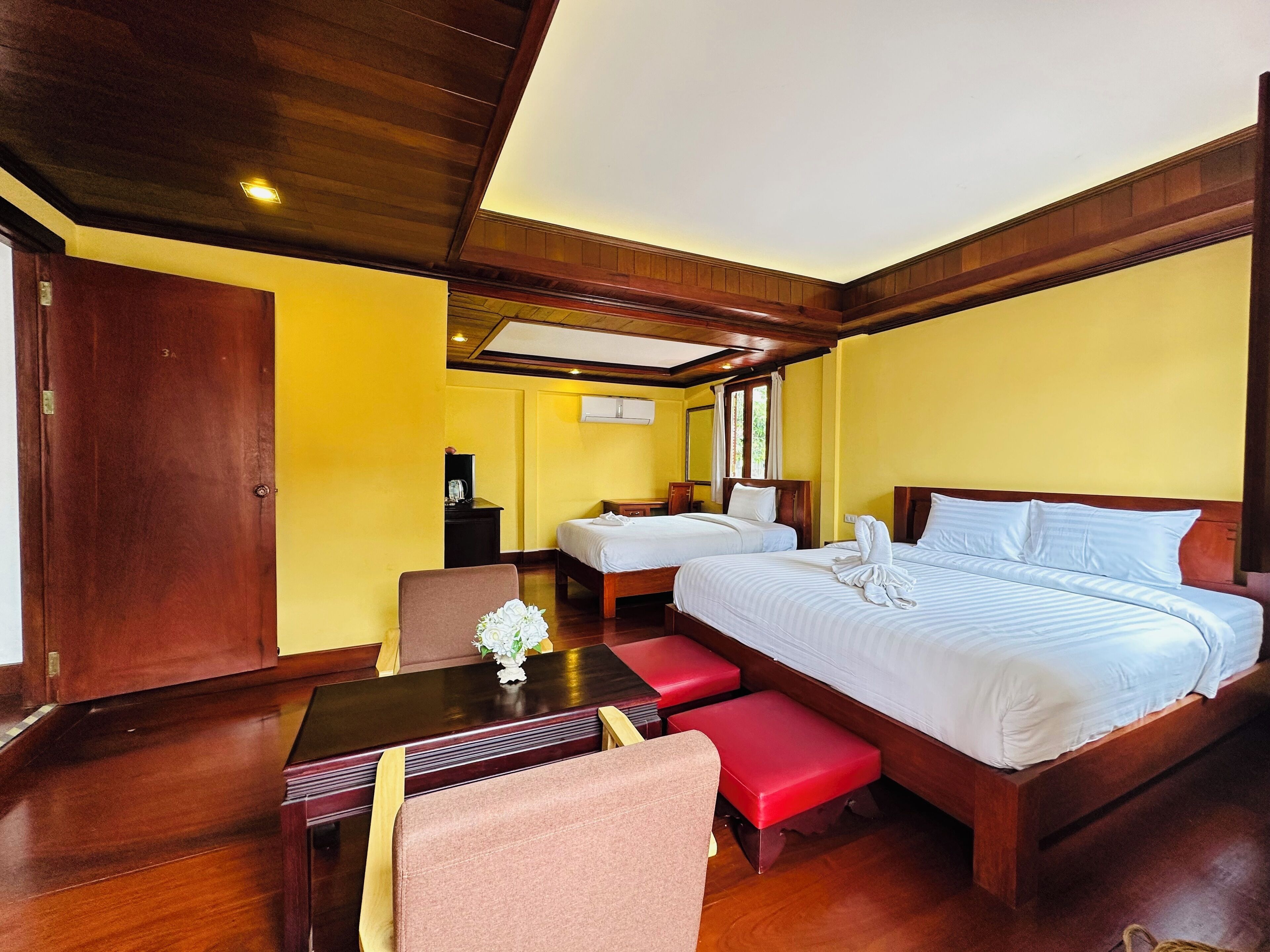 Quarto de hotel com duas camas, uma escrivaninha de madeira, uma cadeira e uma mesa pequena com um vaso de flores.