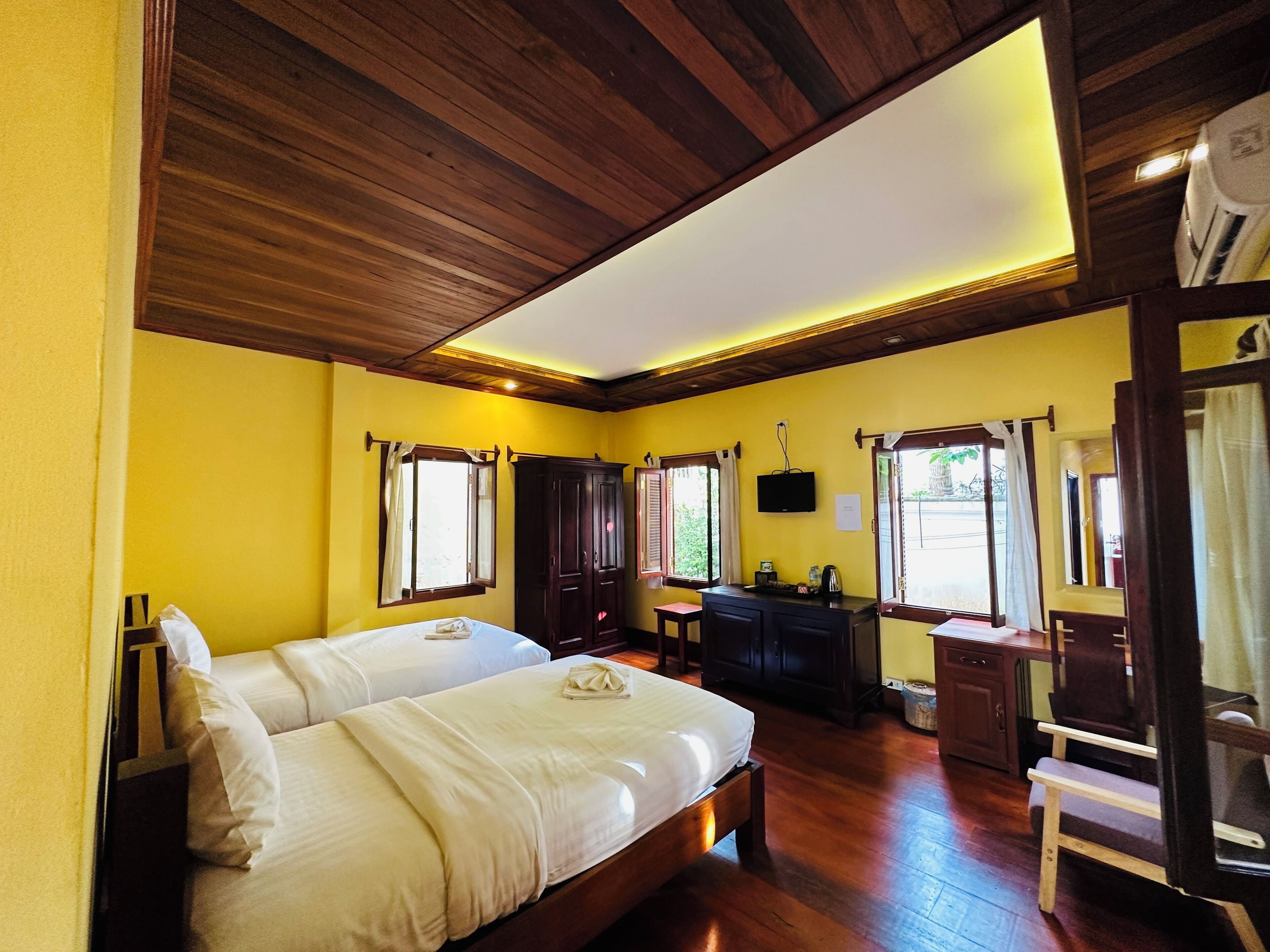 Habitación con dos camas, piso de madera, un escritorio con silla y un televisor en la pared.