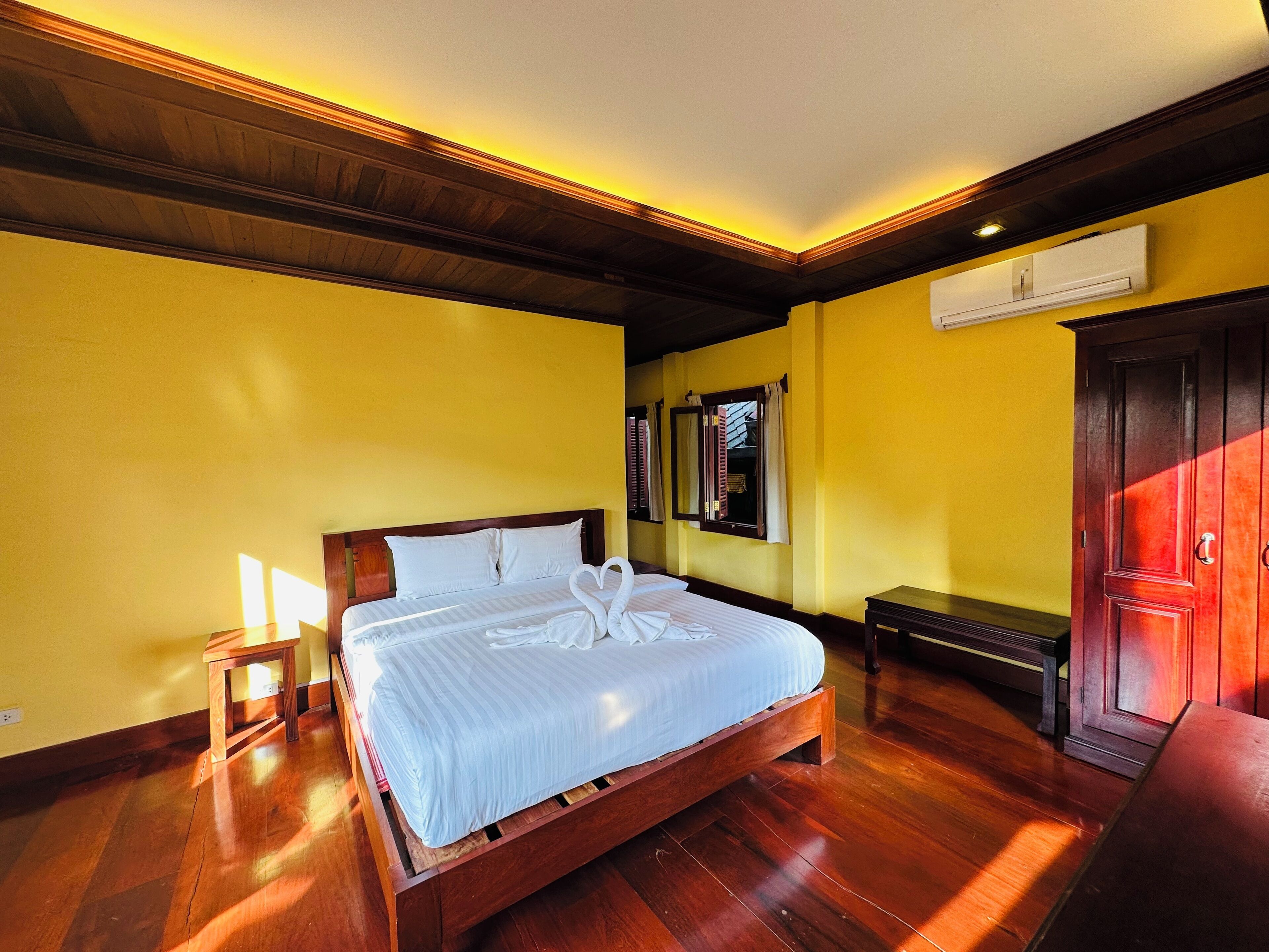 Una habitación de hotel con una cama de madera, paredes amarillas y suelo de madera.