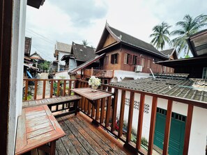 A wooden balcony with a table and chairs, overlooking a traditional house with a tiled roof and a green door. - Villa Phonethip Mekong Riverside (Luang Prabang)