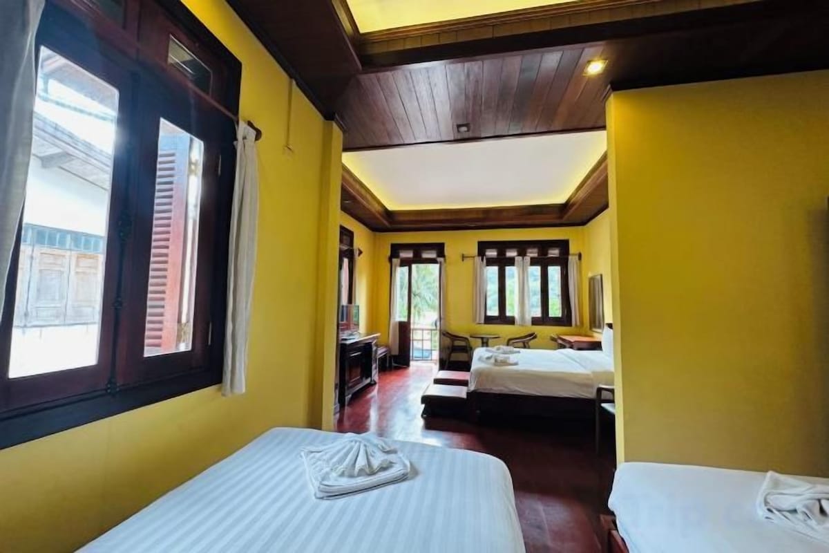 A hotel room with two beds, a wooden ceiling, and a view of the outside.