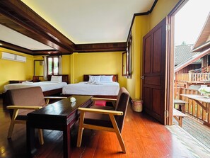 A hotel room with two beds, a wooden table, and a balcony with wooden railings. - Villa Phonethip Mekong Riverside (Luang Prabang)