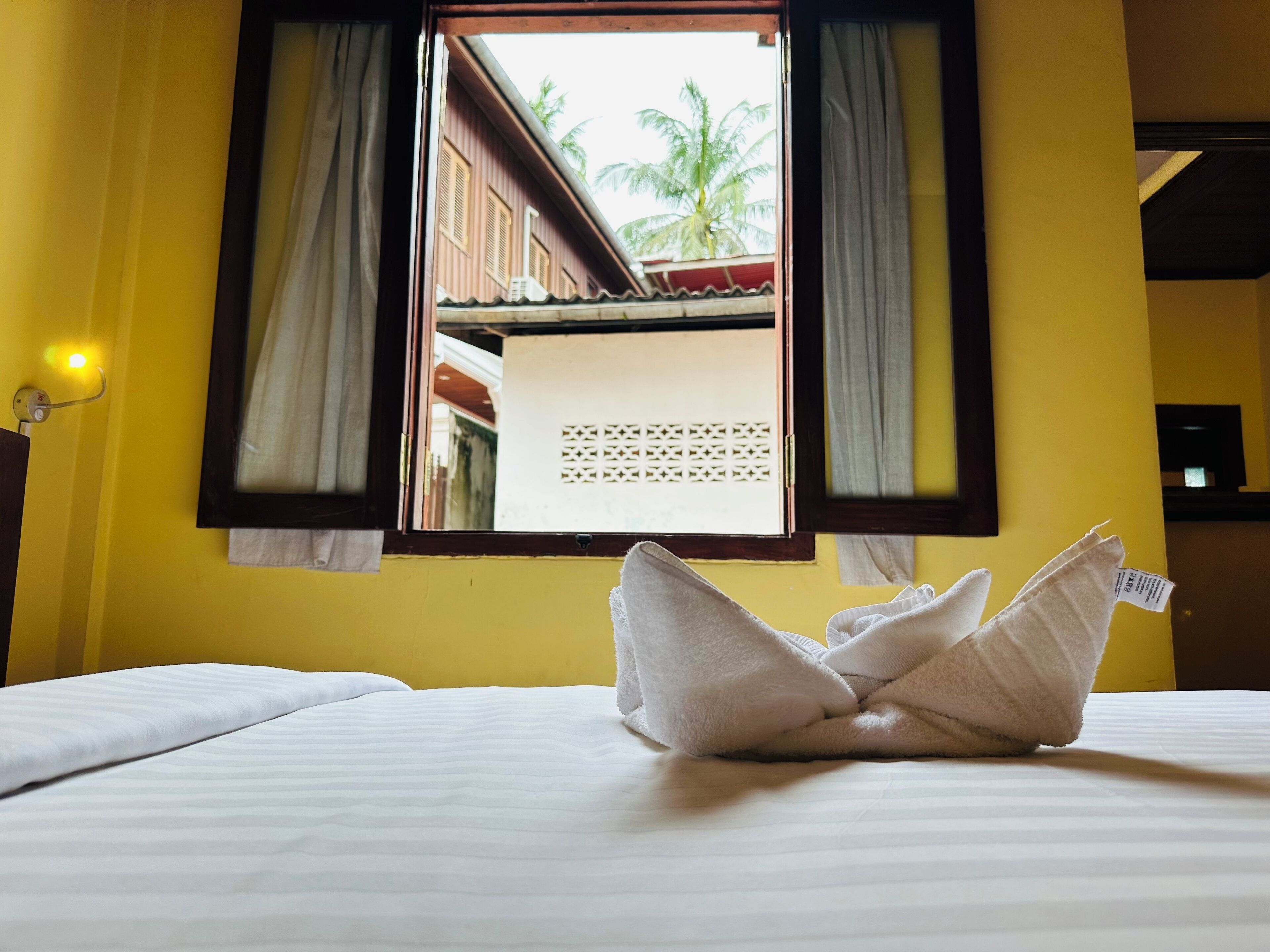 A hotel room with a bed, a window with curtains, and a view of a building outside.