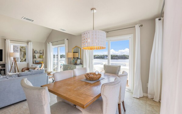 Uma sala de estar ampla com uma mesa de jantar de madeira, assentos confortáveis e uma grande janela com vista para o exterior.