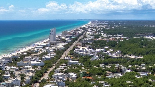 Ein Luftbild einer Küstenstadt mit Strand, Wohngebäuden und einem markanten Turm.