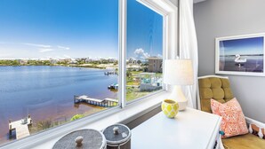 Ein Zimmer mit großem Fenster mit Blick auf ein Gewässer, einer Lampe, einem Kissen und einem gerahmten Bild an der Wand.