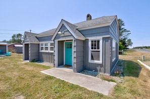 A two-story house with a front porch, a green door, and a small front yard.