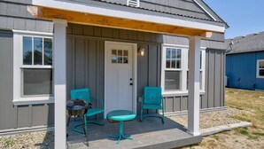 A covered porch with two turquoise chairs and a small table, a white door, and a window on the side of a gray building. - 1Nt. Ok, Walk to Beach and Town, Romantic, Firepit, BBQ (Bungalow2) (Ocean Park)