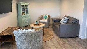 A living room with a grey sofa, a wicker chair, a small round table, and a light blue cabinet. - 1Nt. Ok, Walk to Beach and Town, Romantic, Firepit, BBQ (Bungalow3) (Ocean Park)