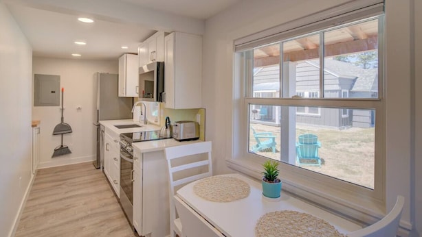 A compact kitchen with white cabinetry, a built-in oven, and a window overlooking a backyard. - 1Nt. Ok, Walk to Beach and Town, Romantic, Firepit, BBQ (Bungalow3) (Ocean Park)