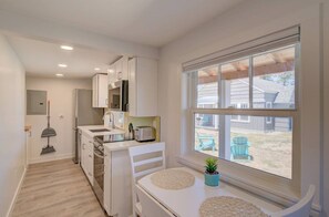A compact kitchen with white cabinetry, a built-in oven, and a window overlooking a backyard. - 1Nt. Ok, Walk to Beach and Town, Romantic, Firepit, BBQ (Bungalow3) (Ocean Park)