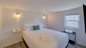 A bedroom with a large bed, white walls, a window, and a bedside table with a lamp. - 1Nt. Ok, Walk to Beach and Town, Romantic, Firepit, BBQ (Bungalow3) (Ocean Park)