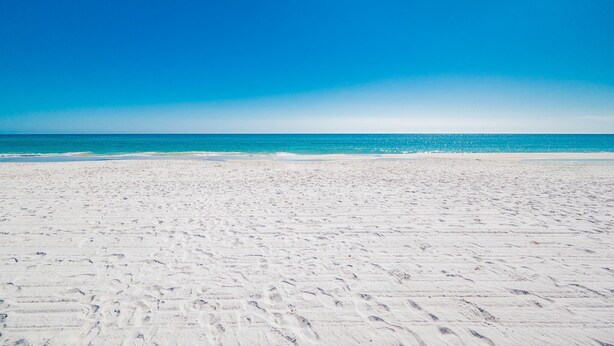 Une vaste plage de sable fin, avec une eau d’un bleu limpide et un ciel dégagé.