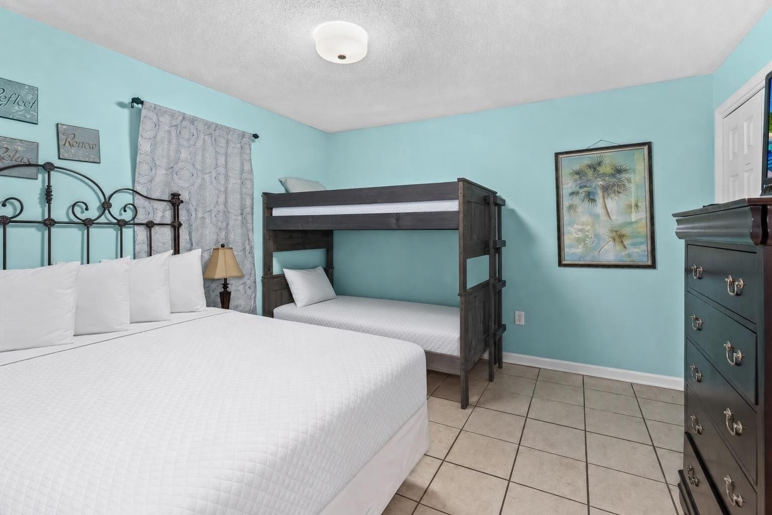 A bedroom with a bunk bed, a single bed, a dresser, and a painting on the wall.