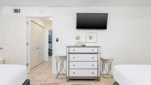 Un dormitorio con dos camas, un aparador, un televisor y una puerta que da a otra habitación.