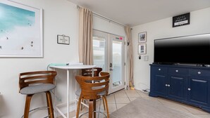 Una habitación con televisión, un armario azul, una mesa blanca, dos sillas de madera y una puerta con ventanal de vidrio corredero.