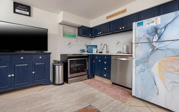Une cuisine moderne avec des meubles de couleur bleu foncé, un four en acier inoxydable, un réfrigérateur au motif marbré et une poubelle.