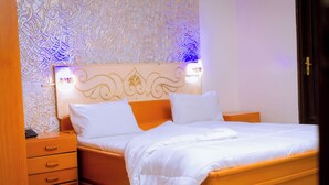 Un letto rifatto con lenzuola bianche, un comodino in legno con cassetti e una parete decorata.