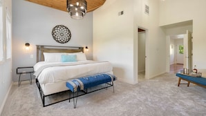 A bedroom with a bed, bedside tables, a bench, a hanging light fixture, and a wall decoration. - The Magnolia House in Old Town - Private Hot Tub (Fort Collins)