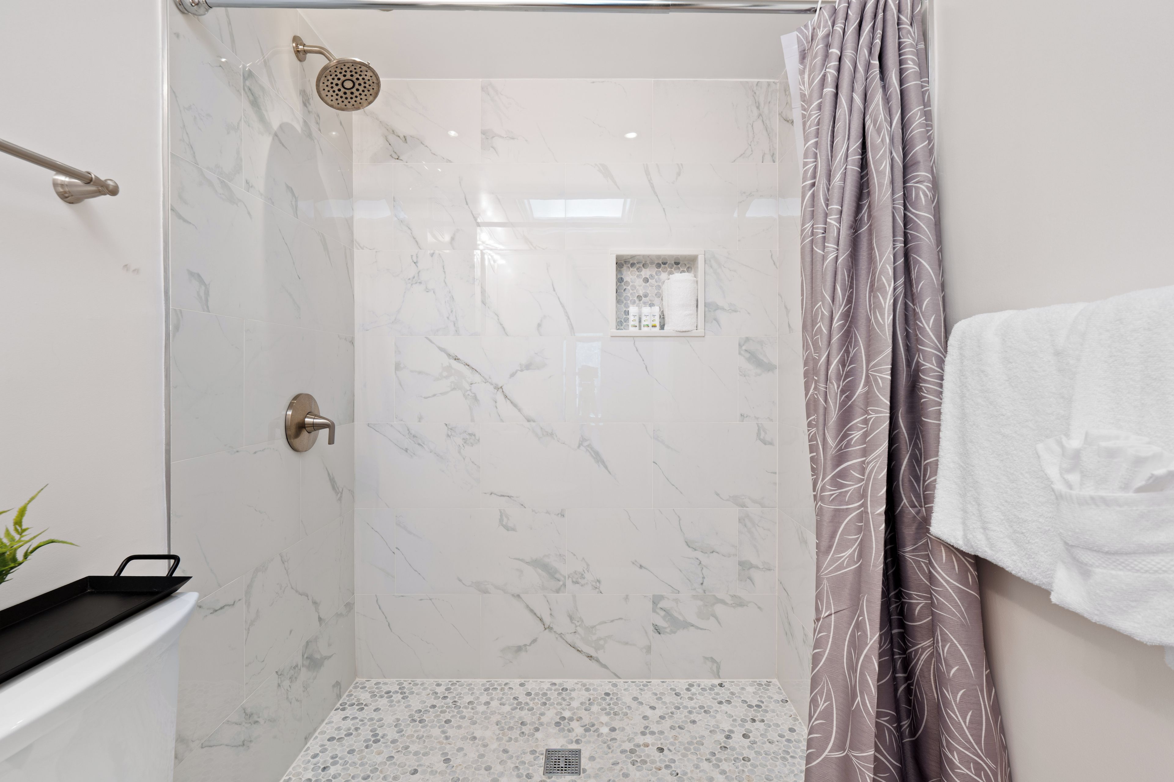 Una doccia con porta in vetro, soffione a mano e portasapone con articoli da toilette.