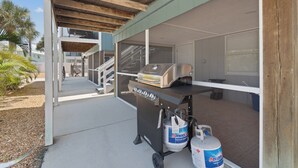 An outdoor patio area with a barbecue grill and propane tanks. - Shared Pool- Beach Bungalow 2 (Fort Myers Beach)