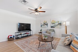 Ein modernes Wohnzimmer mit Flachbildfernseher, Deckenventilator, Sofa, Couchtisch und zwei Bildern an der Wand.