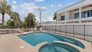 A swimming pool with a curved design, surrounded by a fence, and adjacent to a building with multiple windows. - Shared Pool- Beach Bungalow 2 (Fort Myers Beach)