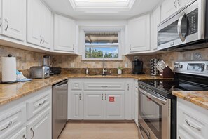 A modern kitchen with white cabinetry, granite countertops, a built-in microwave, and a window with a view of trees.