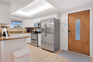 Een moderne keuken met witte kasten, roestvrijstalen apparatuur en een houten deur met een decoratief glasraam.