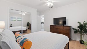 A bedroom with a bed, a dresser, a television, a ceiling fan, and a potted plant. - Shared Pool- Beach Bungalow 2 (Fort Myers Beach)