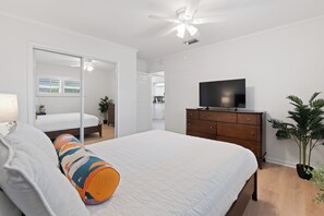 Ein Schlafzimmer mit einem Bett, einem Schminktisch, einem Fernseher, einem Deckenventilator und einer Topfpflanze.