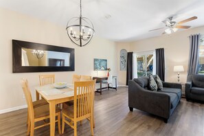 A dining area with a wooden table and chairs, a chandelier, and a large mirror on the wall.
